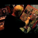 Electronic musician adjusting a densely wired modular synthesizer rig