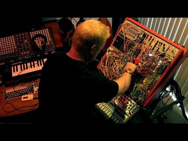 Electronic musician adjusting a densely wired modular synthesizer rig