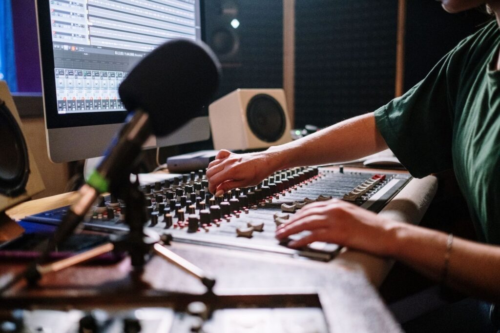 Audio engineer adjusting a mixing console beside a computer waveform display