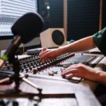 Audio engineer adjusting a mixing console beside a computer waveform display